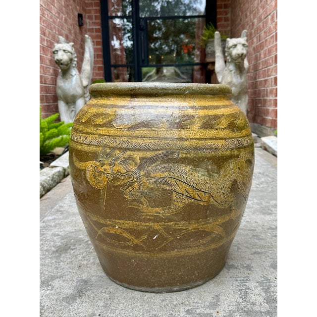 Antique ceramic pot featuring an intricately carved or embossed dragon motif. The pot has a rich, earthy glaze in shades...