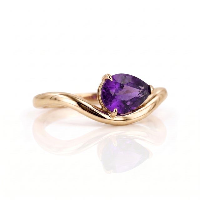 Discover the captivating beauty of this deep purple, pear-shaped Amethyst ring. The 7x5mm gemstone is the centerpiece of a...