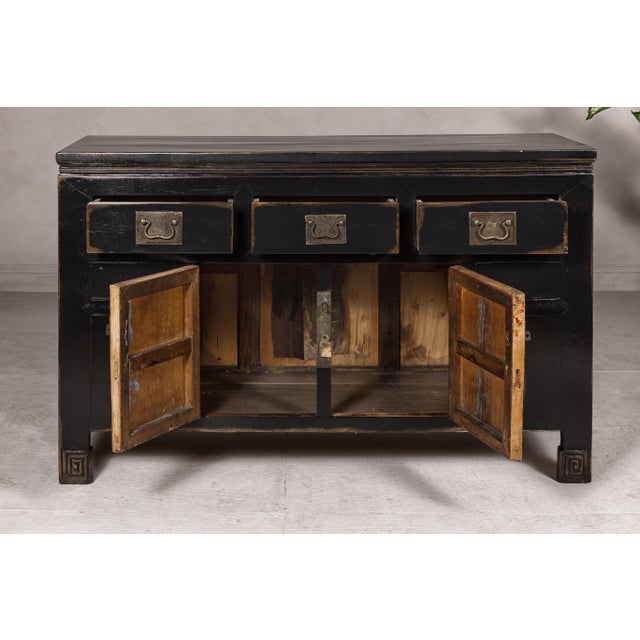 A black lacquered Qing Dynasty sideboard from the 19th century with rubbed edges, brass hardware, three drawers over two...