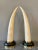 A pair of tall faux tusks in tessellated marble mounted on dark marble plinths with brass accents. A tessellation or...
