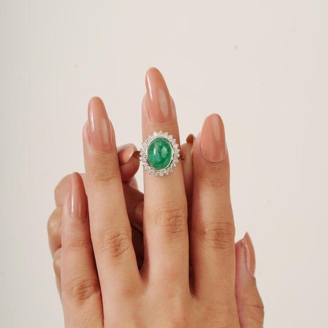 Featuring a oval cabochon emerald weighing 5.2 carats, The center stone is surrounded by a halo of accent stones weighing...