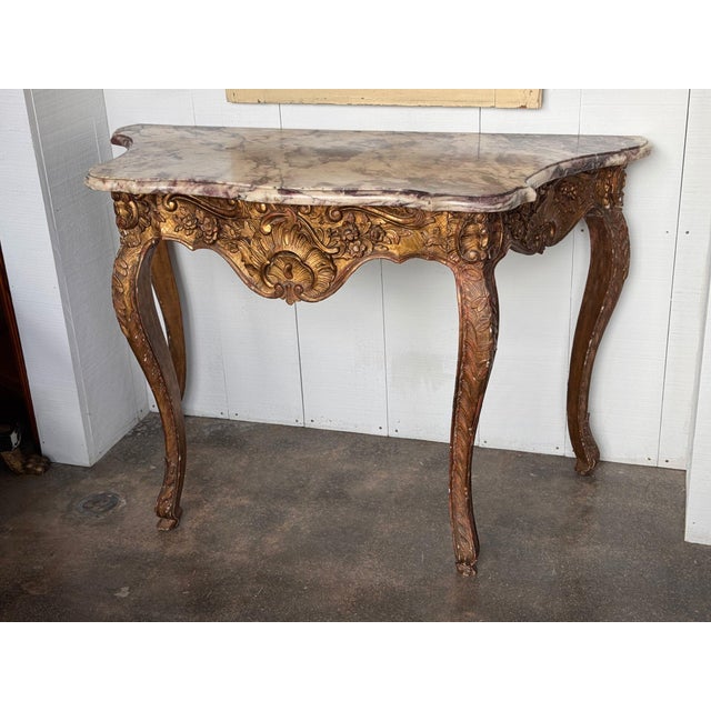 18th century Italian giltwood console, carved and gilded throughout, with a shaped marble top in cream veined with plum...