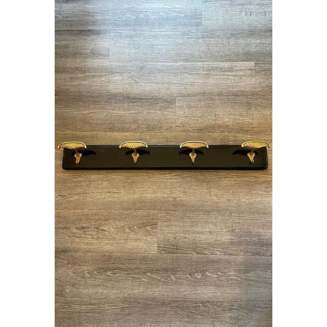 1950s ebonized wood coat rack with four brass knobs. Each knob features a gridded decorative motif and its own integrated...