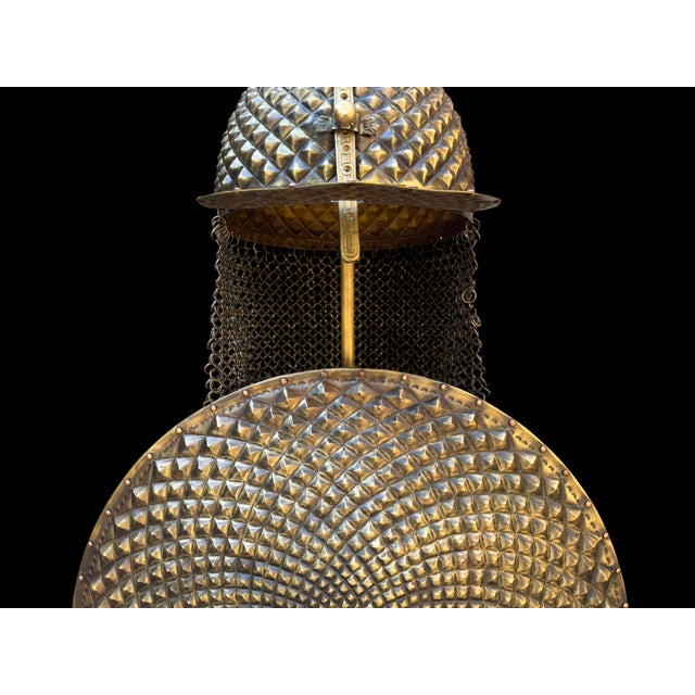 A domed helmet and a round shield rise together from a shared hammered stand, every surface raised entirely by hand into a...