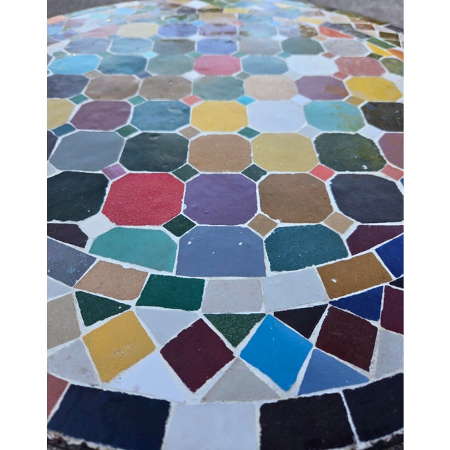 Beautiful round mosaic tile table featuring a vibrant multicolor tiled top and durable black wrought-iron style base. The...