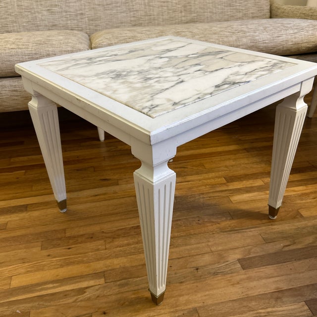 Modern glam white painted wood side table with fluted legs capped with brass ferrules at the bottom. The top is Carrara...