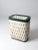 An antique woven hamper with a white basket body accented by painted green detailing. The wood-framed lid opens on a rear...