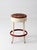 Vintage mid-century industrial stool featuring a cream-painted metal frame, red circular footrest, and upholstered seat....