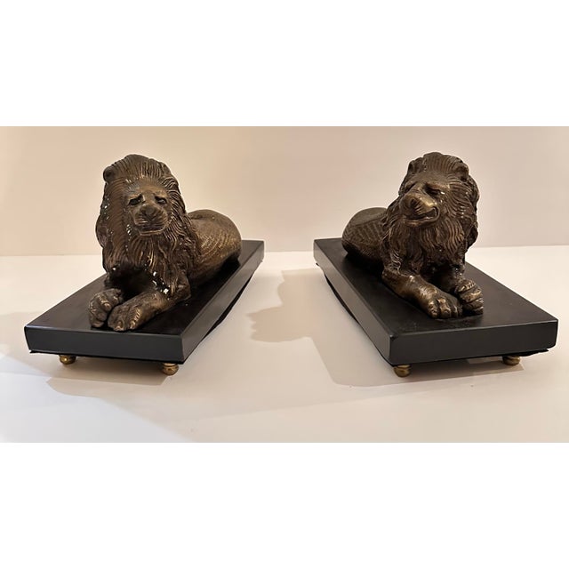 A pair of lions stretched out in full repose, paws crossed out in front, manes rendered in deep channeled lines that catch...