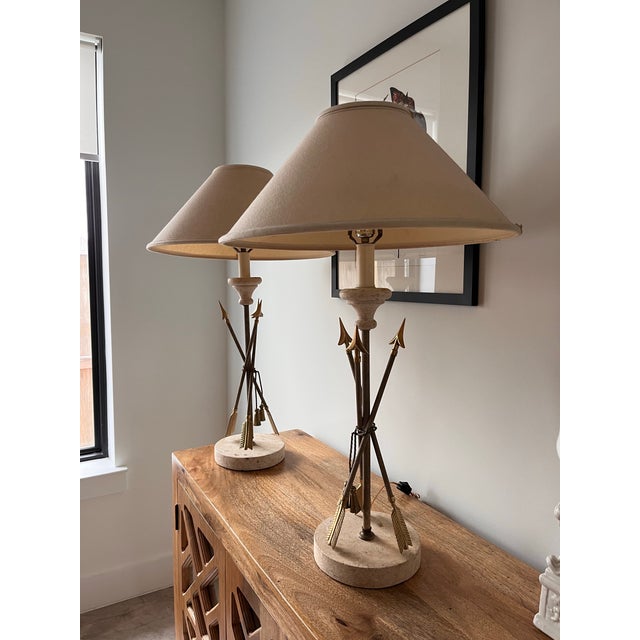A beautiful pair of French brass and travertine arrow and tassel table lamps. Vintage fabric shades are included. Both...