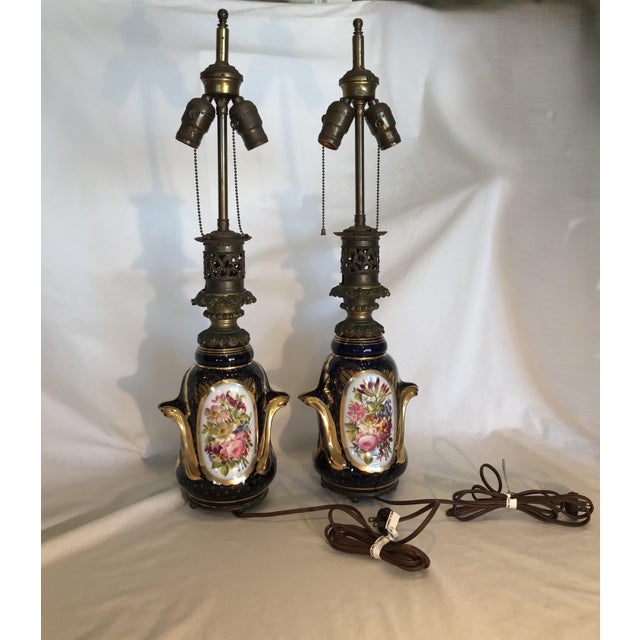 Lamps have cobalt blue bodies and each side is illustrated with a unique hand-painted floral cartouche. Each lamp has...