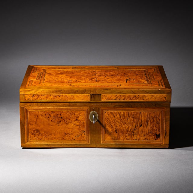 Small Biedermeier casket with framed burl veneer panels. with brass side handles and lock with key. The interior is paper-...