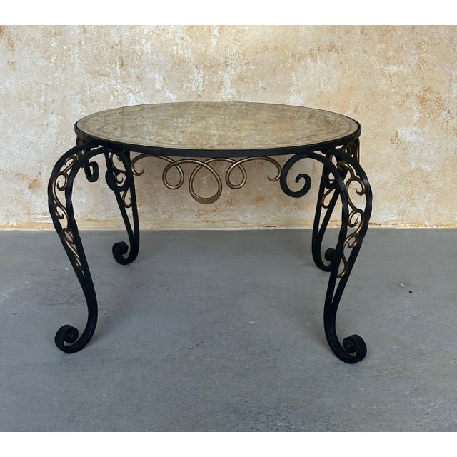 An interesting 1940s French iron coffee table with a decorative reverse painted mirror top. The elegantly scrolled base...