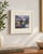 Framed decorative print of a lakeside garden with blooming flowers, water and soft mountain views in blues, greens,...