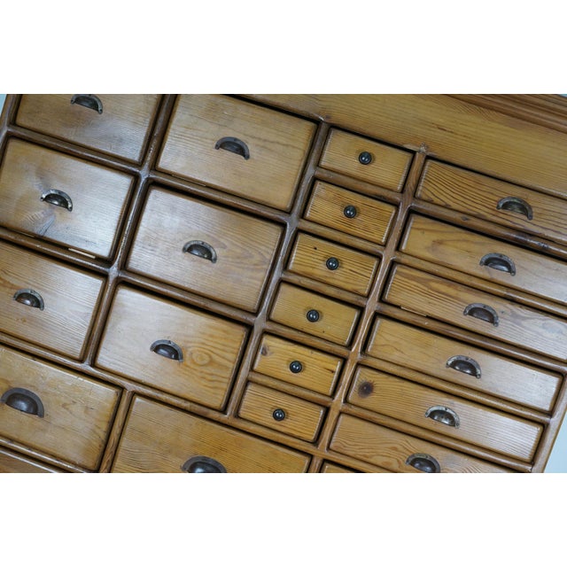 This apothecary cabinet was made in The Netherlands from antique pine. It features 29 drawers with nice patinated metal...