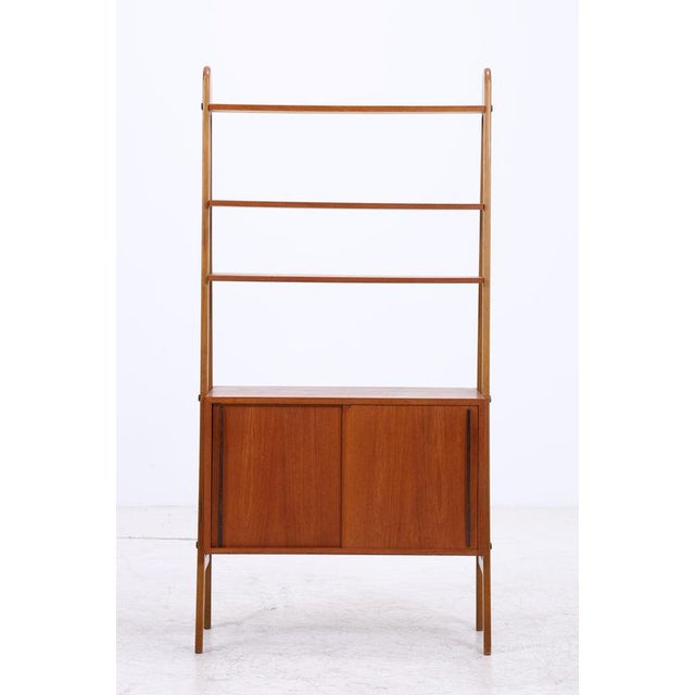 Vintage teak shelving unit with a delicate construction and a closed storage compartment at the bottom. Three open shelves...