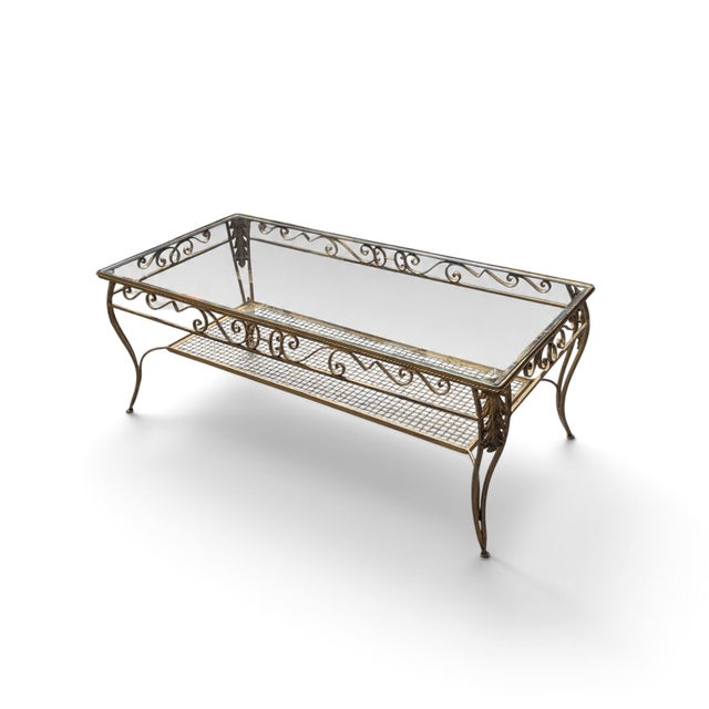 An estimated late-20th-century rectangular coffee table pairing a clear glass top with an ornate gold-toned metal frame....