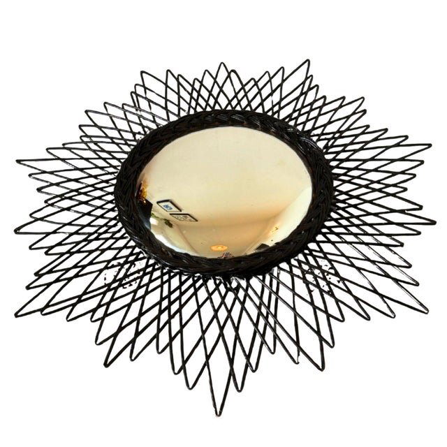 A striking french sunburst mirror from the 1950s, hand-woven in ebonized wicker with bold, radiating spikes. Its convex...