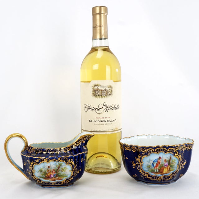 A beautifully hand painted rococo-style porcelain creamer and open sugar bowl set with cobalt blue ground, gold gild, and...