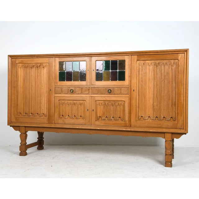 Oak sideboard with carved linenfold-style panels to the cabinet doors and drawers, raised on turned legs. The case...