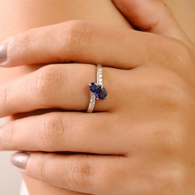 This modern 14K white gold bypass ring showcases two pear-cut natural blue sapphires totaling approximately 0.66 carats....
