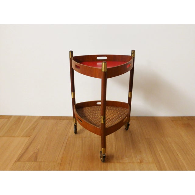 Trolley consisting of three teak legs with brass details, two service tops, the upper one in red laminate, the lower one...