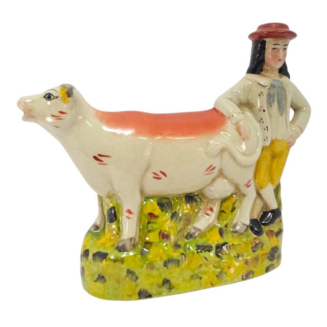This Staffordshire cow and boy figurine is a substantial English Staffordshire-style earthenware flatback with the warmth...