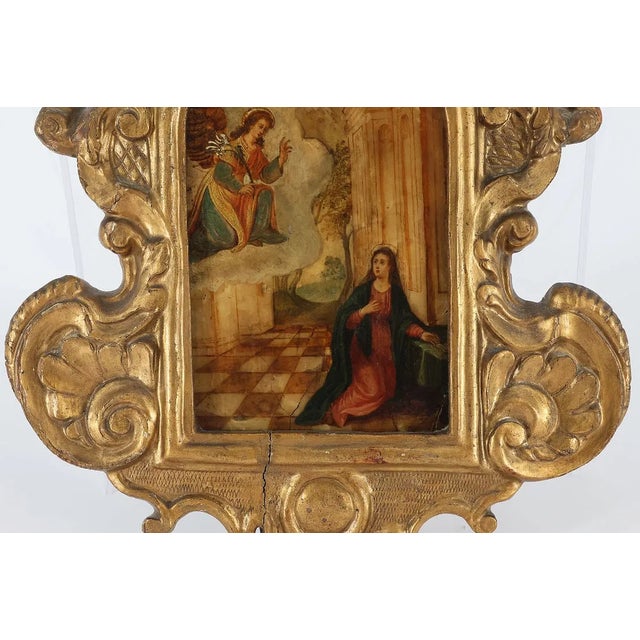 A compelling 17th-century Annunciation scene by an unknown master, presented within an elaborate hand-carved giltwood...
