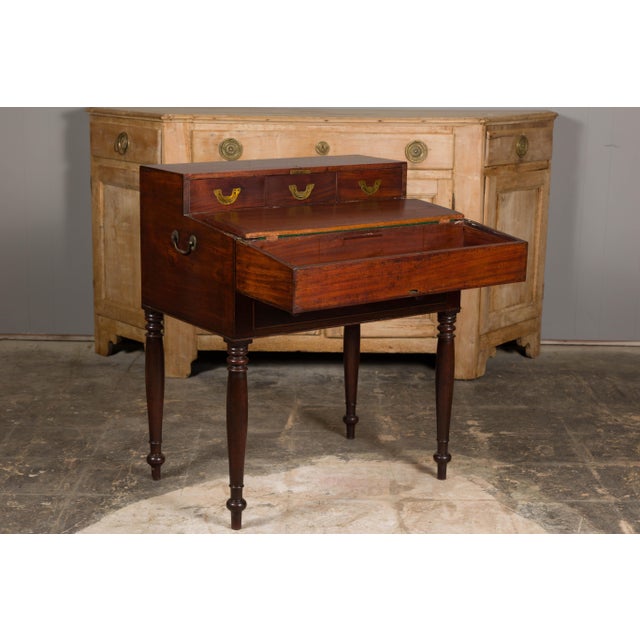 An English mahogany campaign period box on legs from the 19th century revealing a desk with drawers and green felt. This...