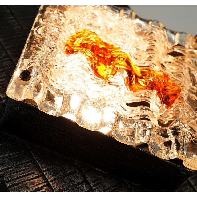 A distinctive wall lamp made of grey wrought iron with a textured finish and delicate filigree glass featuring amber-...