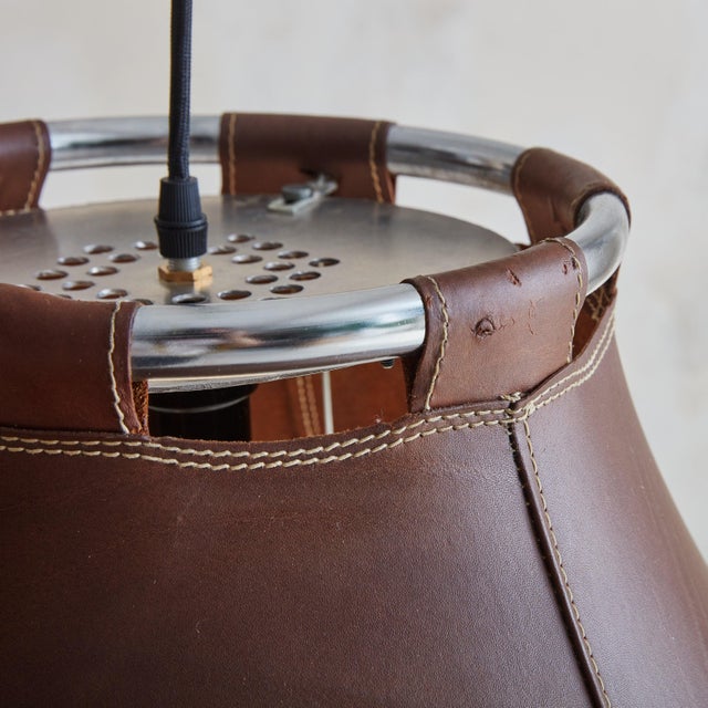 A 1970s Swedish pendant light featuring a circular chrome frame encircled by a rich, deep brown leather shade with stitch...