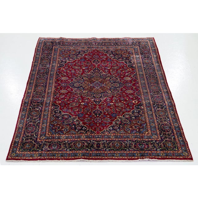 This vintage Persian Kashan has a red and blue field adorned with multicolor accents all over the design. This rug...