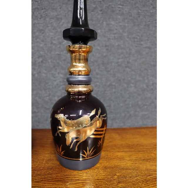 Striking pair of royal purple art glass decanters featuring elaborate gilt horse decoration with botanical and geometric...