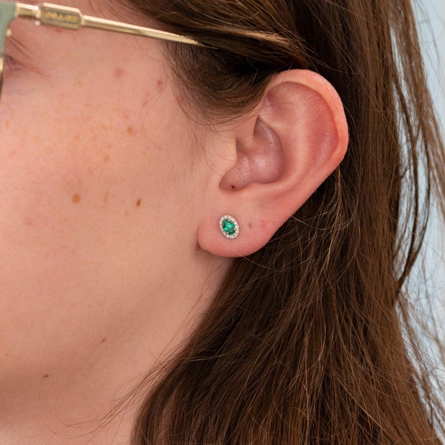 Vivid emeralds glow within a brilliant halo of diamonds in these oval stud earrings, set in solid 14K white gold. The...