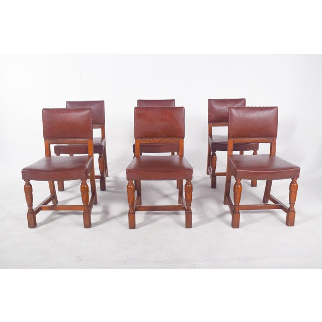 Six chairs with brown leather backs and seats. The chairs are simple but elegant in style, with metal nails decorating and...