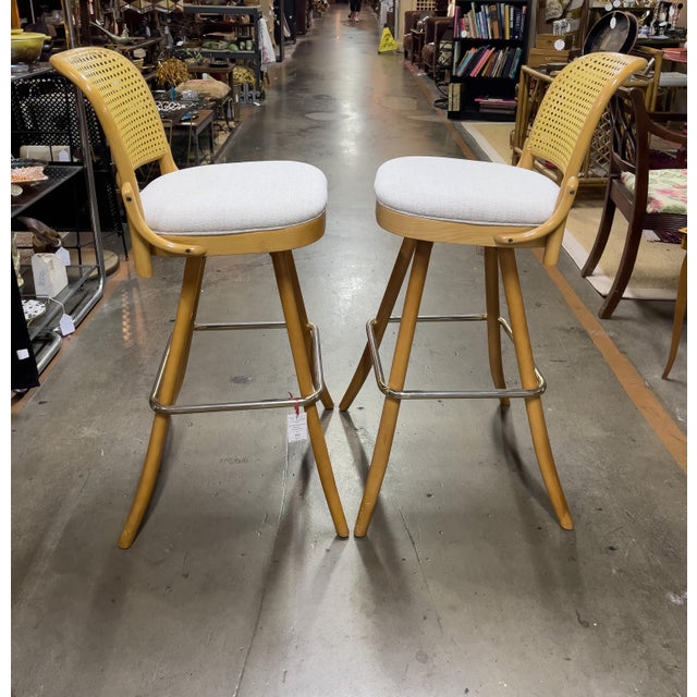 A pair of bentwood swivel barstools with upholstered seat and cane (plastic) backrest fabricated in 1995. The footrest is...