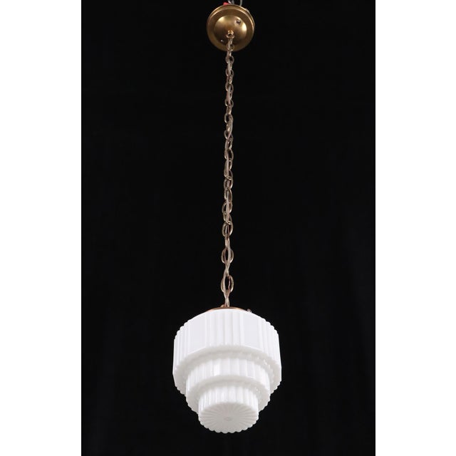 Art Deco pendant light with a tiered white opal glass shade with scalloping details. This requires one standard Edison...