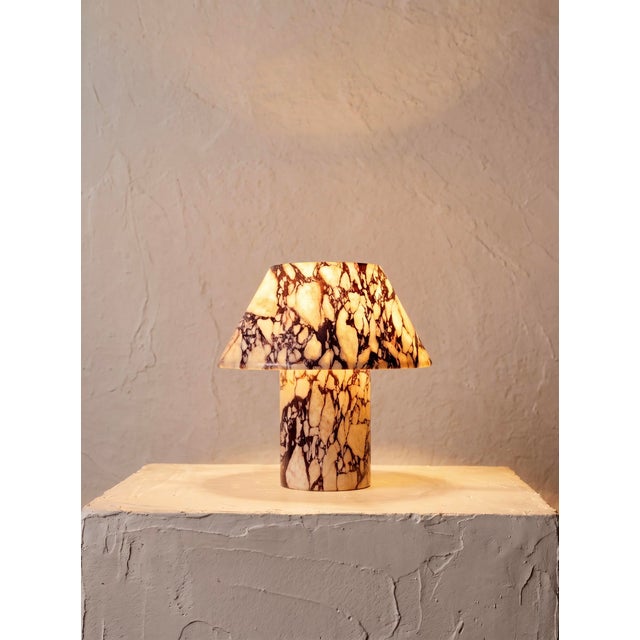 A sculptural mushroom-form table lamp hand-carved from solid Calacatta Viola marble, a rare Italian stone prized for its...