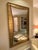 A dramatic Hollywood Regency-style wall mirror, measuring an impressive 65" x 39". The frame is richly textured gold leaf...