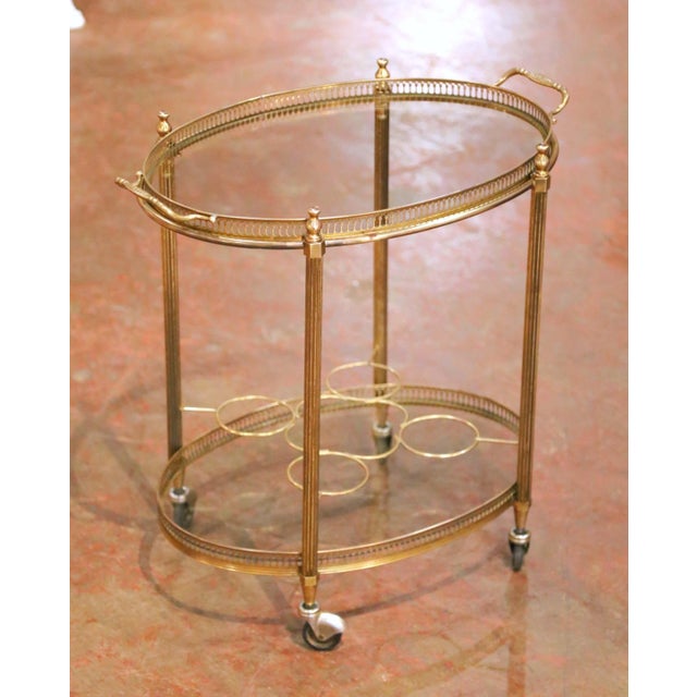 Crafted in France circa 1960, this elegant mid-century brass bar cart features a refined neoclassical design with a light...