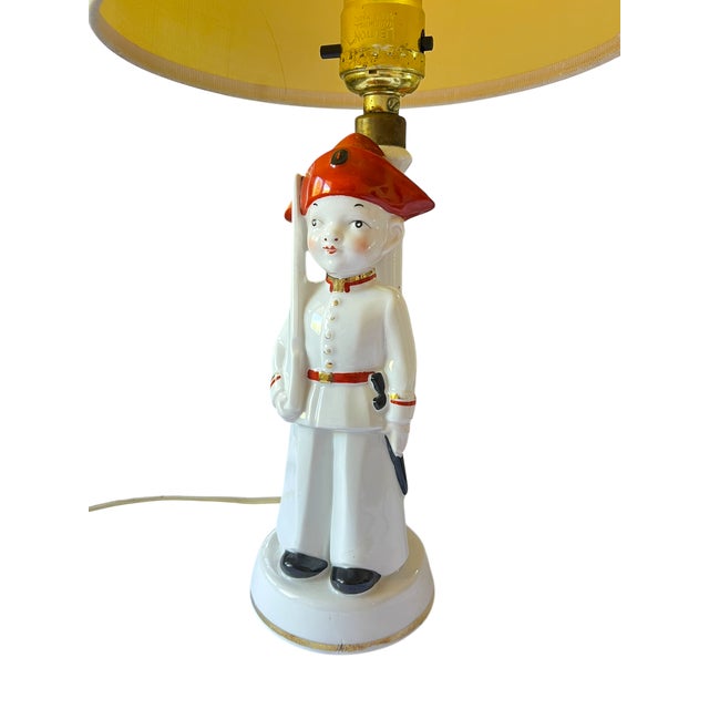 Charming vintage porcelain figural table lamp featuring a stylized child soldier in uniform, rendered in glossy white with...