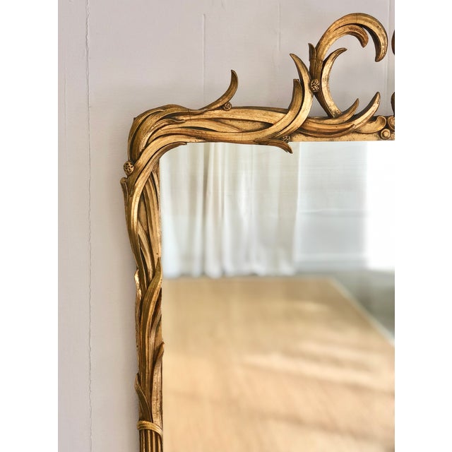 Ornate vintage to antique mirror featuring a gilt finish with scrolled motifs, floral accents, and reed detailing...
