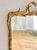 Ornate vintage to antique mirror featuring a gilt finish with scrolled motifs, floral accents, and reed detailing...