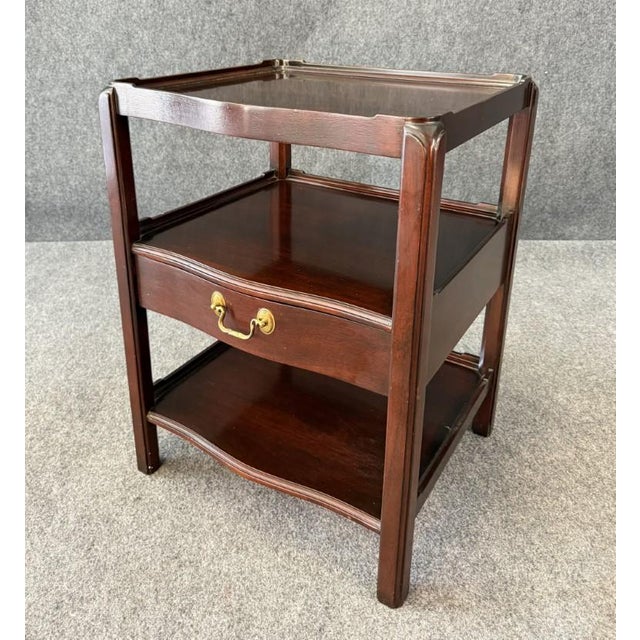 This Wellington Hall mahogany side table features a refined two-tiered design with gently shaped shelves and a single...