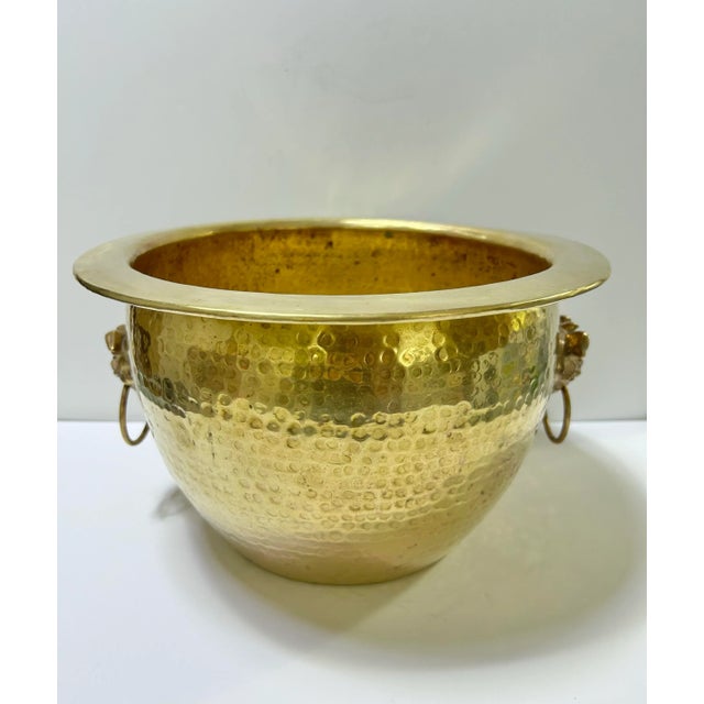A striking vintage hammered brass cachepot featuring sculptural foo dog ring handles. The Asian motif paired with warm...