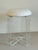 A lucite low stool with vinyl upholstered seat. The ribbon-like clear acrylic legs cross in at the base. The padded round...