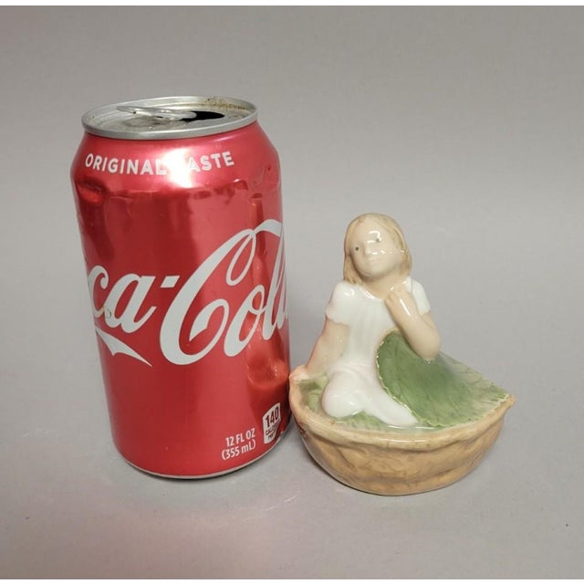 A charming mid-century Royal Copenhagen porcelain figurine depicting Thumbelina nestled inside a walnut shell. Hand-...