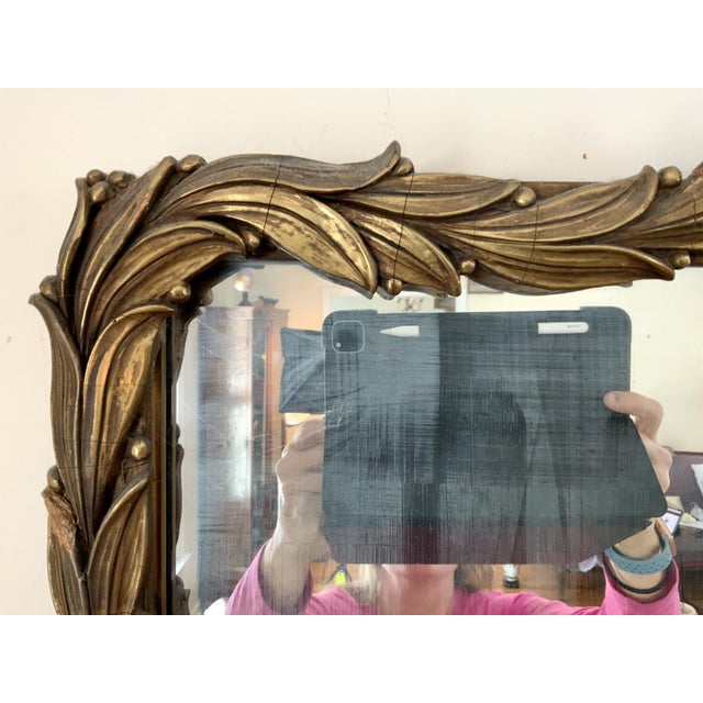 Ornately carved French Rococò style gilt wood rectangular wall mirror with a warm aged gold finish, softly arched top...