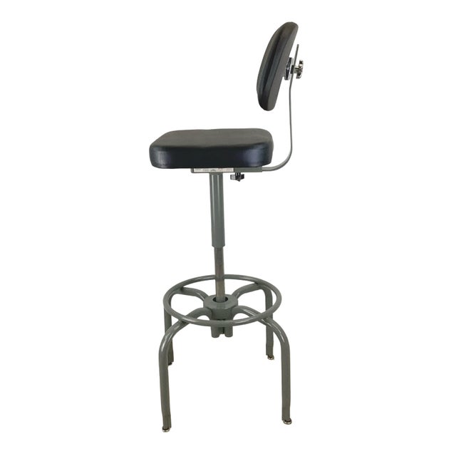 A vintage American industrial drafting stool featuring an adjustable-height pedestal, upholstered seat and backrest,...