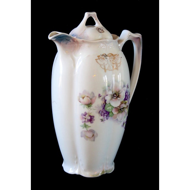 A charming vintage porcelain chocolate pot featuring a delicate floral motif in soft lavender, green, and white tones. Its...